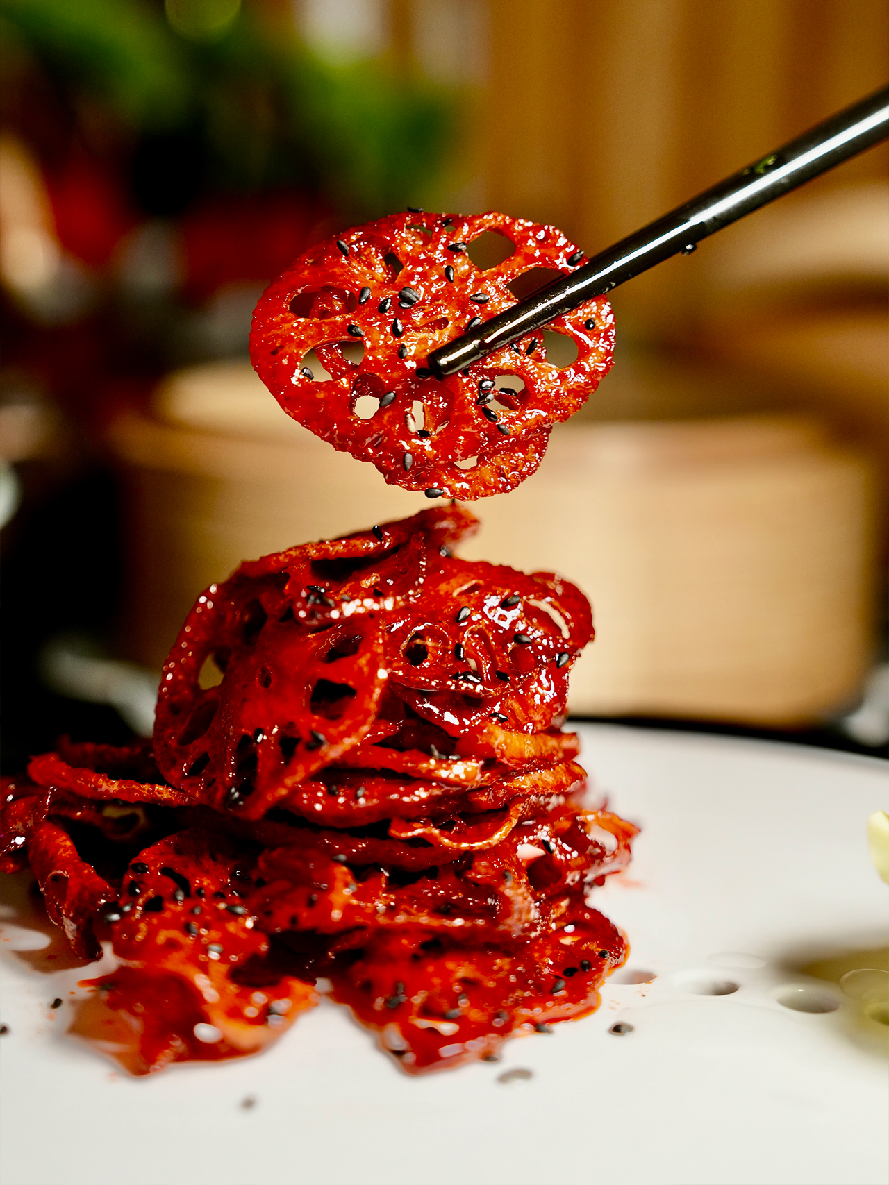 Floral-Chinese-Restaurant-New-York Stack of spicy, glazed lotus root slices sprinkled with black sesame seeds. Chopsticks hold one slice aloft.