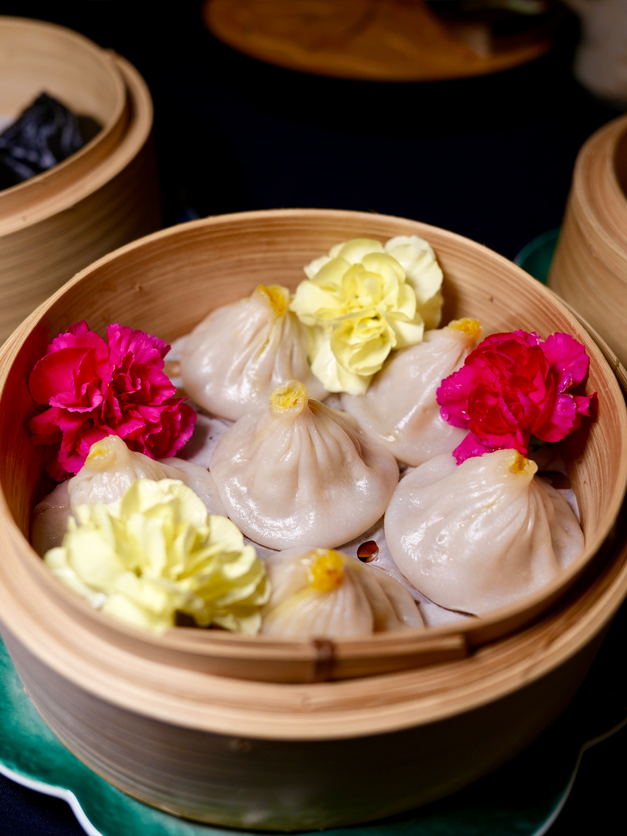 Floral-Chinese-Restaurant-New-York Steamer basket with delicate soup dumplings (xiao long bao) topped with a yellow accent and decorated with pink and yellow flowers.