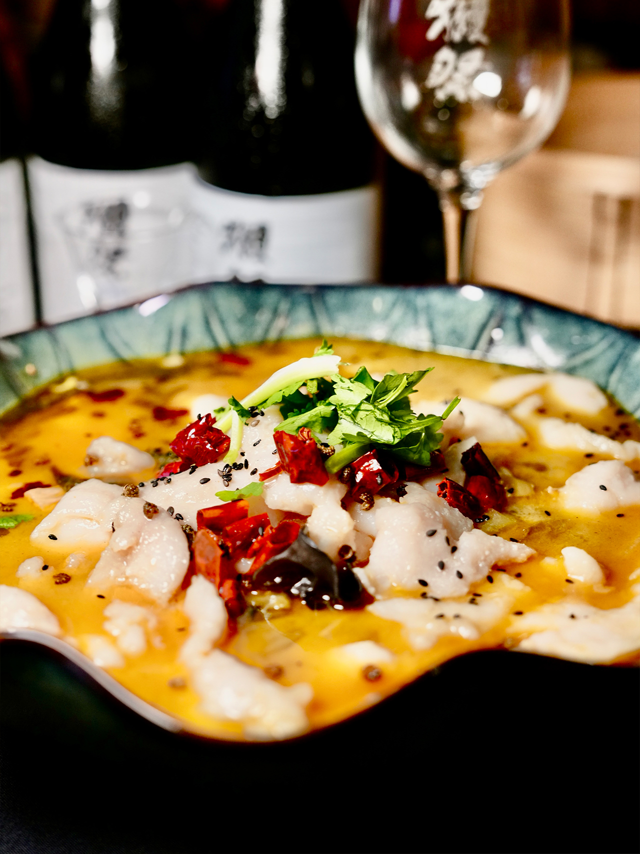 Floral-Chinese-Restaurant-New-York A bowl of spicy fish fillets in a vibrant yellow chili oil broth, garnished with cilantro, red peppers, and black sesame.