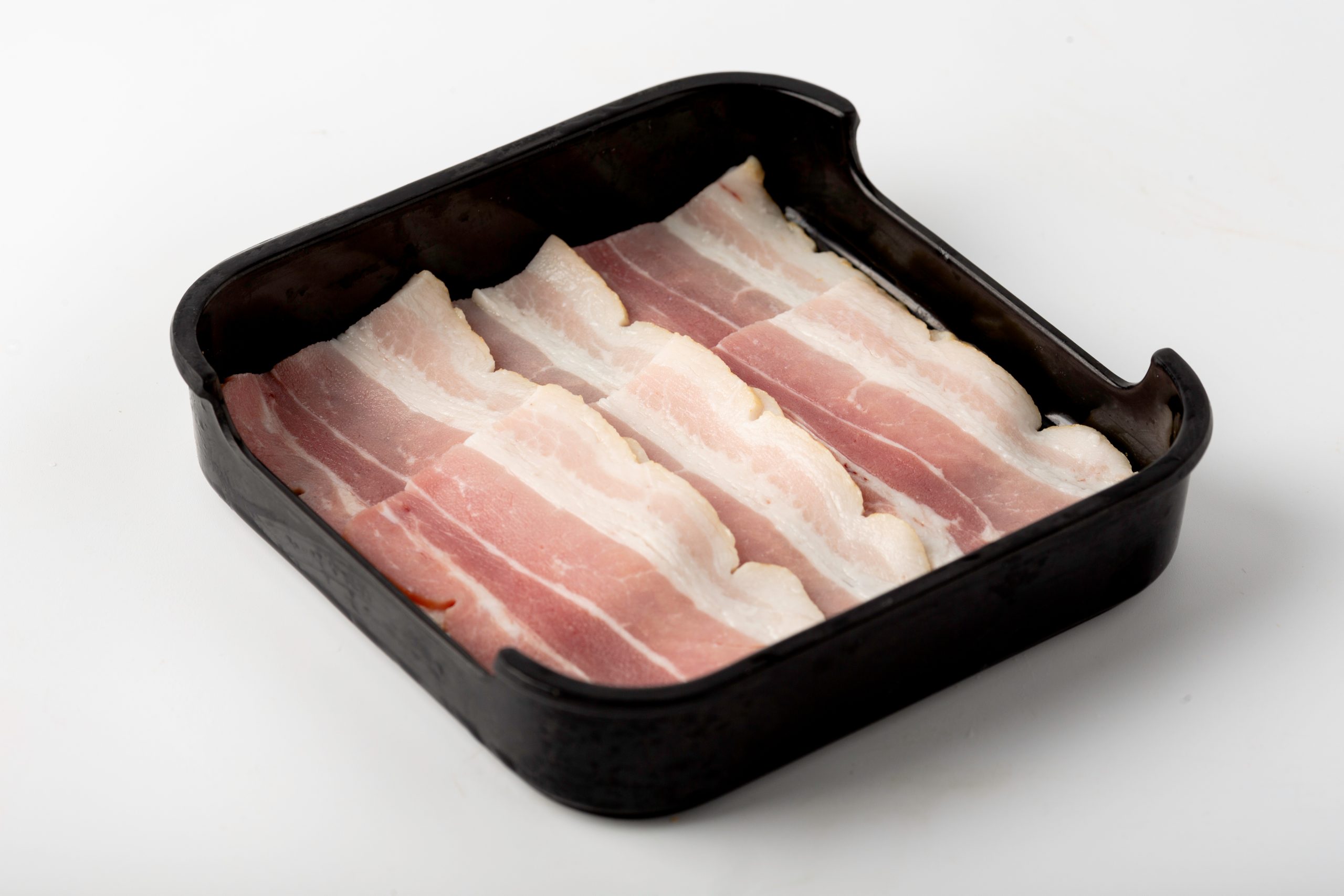 Fresh bacon slices neatly arranged in a black tray at Firestone Hotpot & BBQ Restaurant in Tallahassee