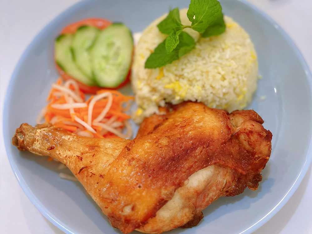 `Fried chicken leg with rice, cucumber, tomato, and pickled vegetables on a plate`