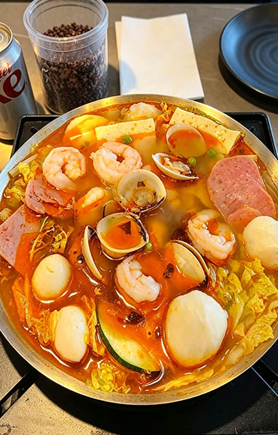 Close-up of seafood hot pot ingredients: shrimp, clams, fish balls, tofu, and vegetables in a bubbling spicy broth
