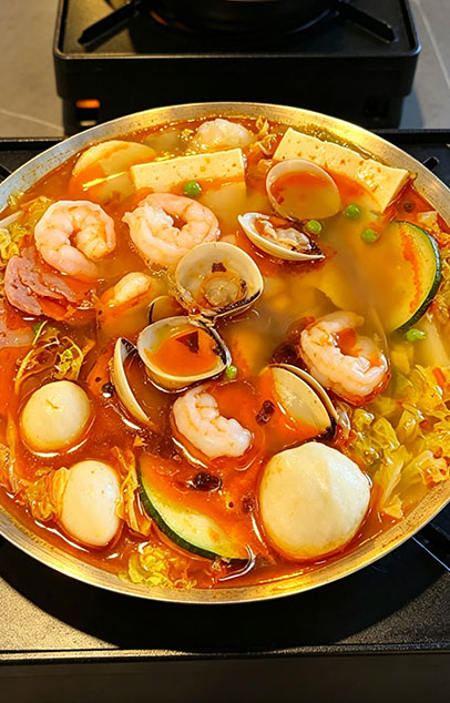 Seafood hot pot with shrimp, clams, fish balls, luncheon meat, tofu, and cabbage in a spicy broth