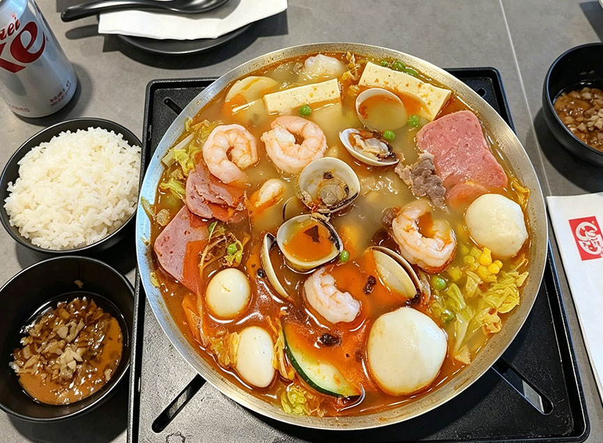 Seafood hot pot with shrimp, clams, fish balls, and luncheon meat, paired with rice, dipping sauce, and a Coca-Cola