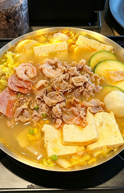 Beef and seafood hot pot with sliced beef, shrimp, luncheon meat, tofu, zucchini, fish balls, and cabbage in a light yellow broth
