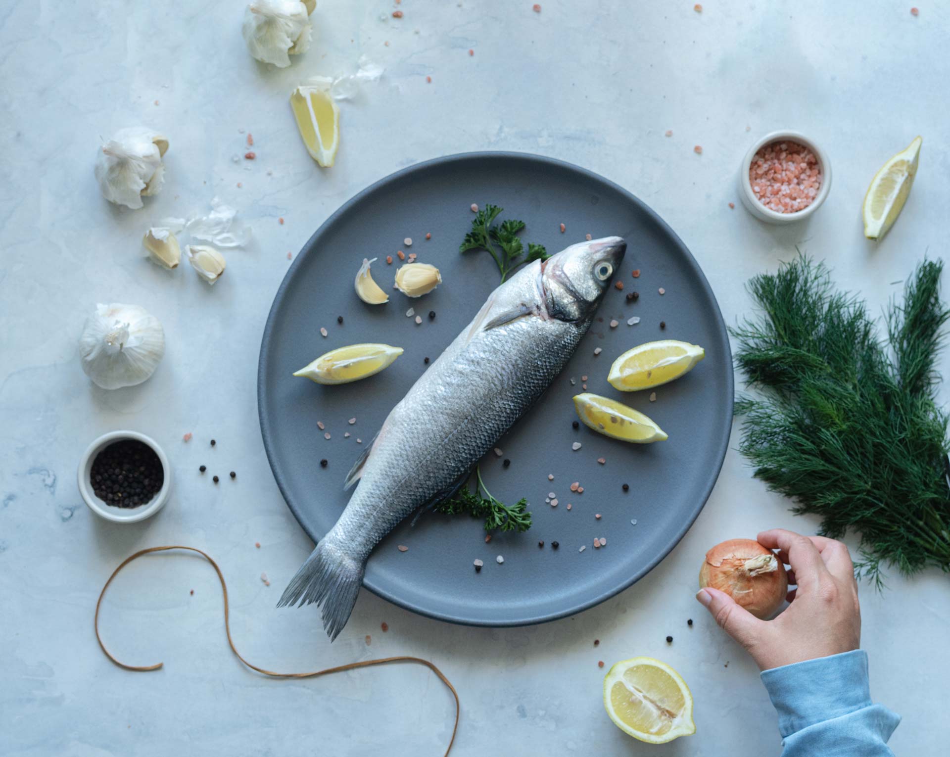 Raw whole sea bass on grey plate with lemon, garlic, herbs and seasonings