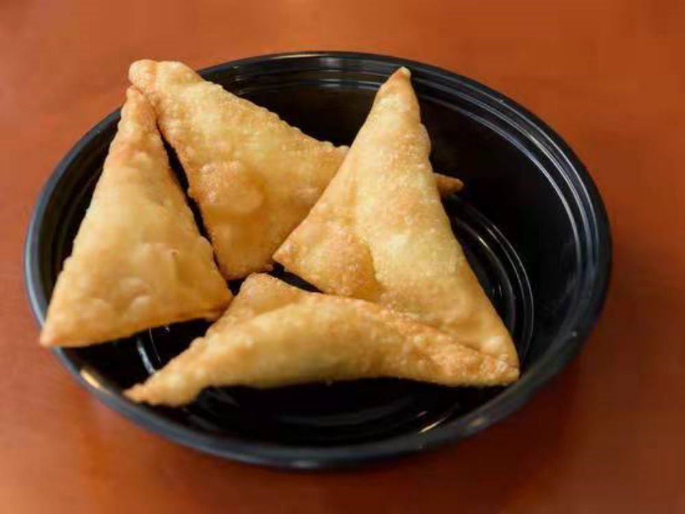 Four crispy fried samosas in black plastic bowl