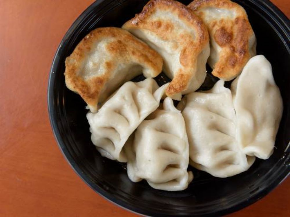 Pan-fried and boiled dumplings in black takeout bowl