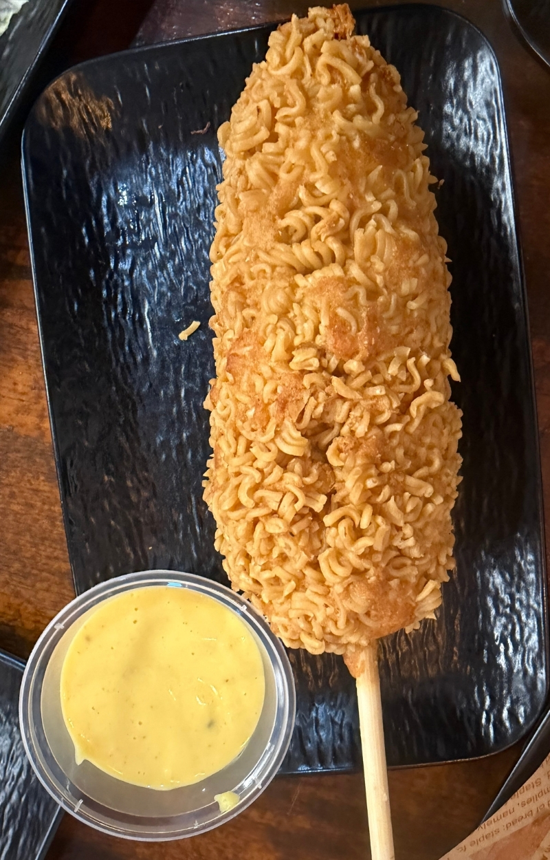 Crispy corn dog coated with whole ramen noodles and dipping sauce at Gangnam Crispy, a Korean Restaurant in Toledo