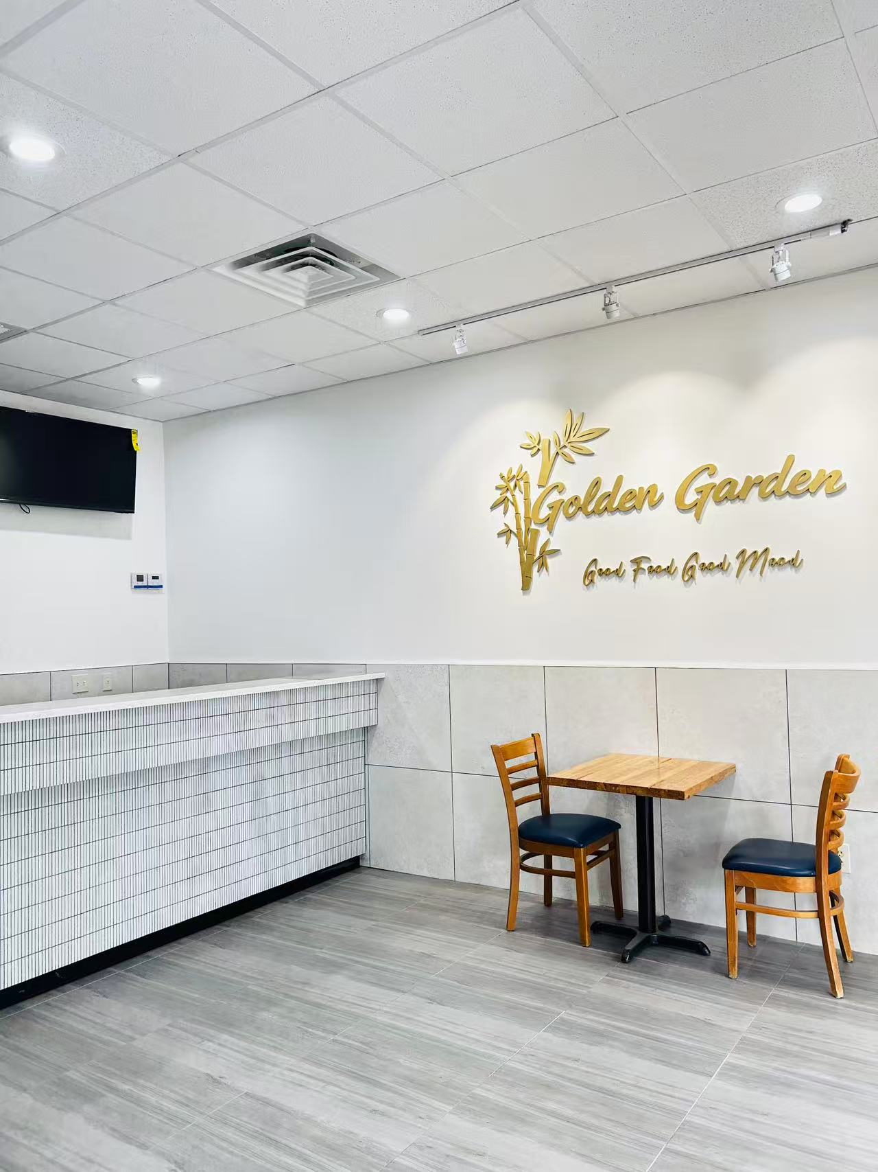 Bright dining area with Golden Garden bamboo logo wall and small wooden table set at Golden Garden, a Chinese Restaurant in Pompton Lakes