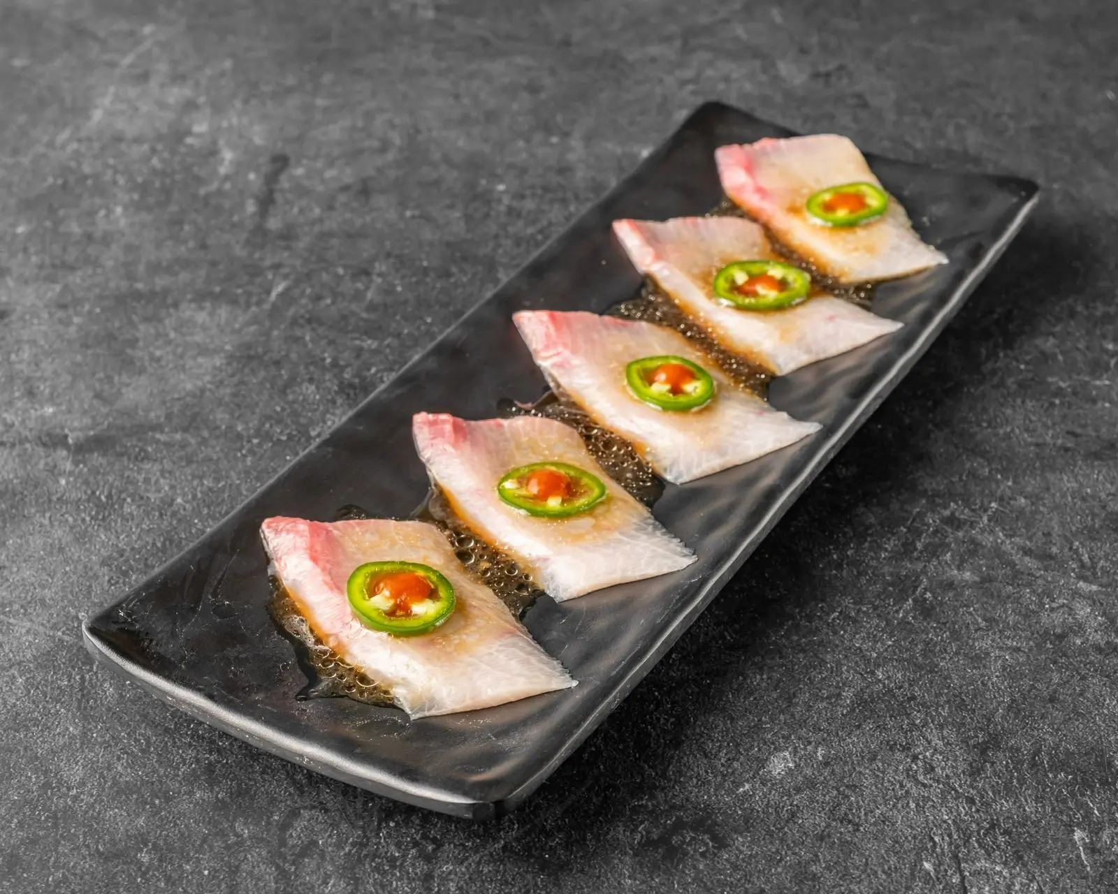 Fresh sashimi topped with jalapeno slices and sauce at Niku Sushi, a Japanese restaurant in Anaheim