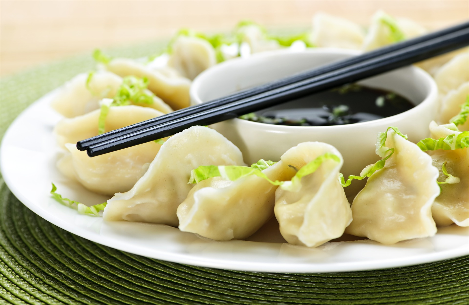 Steamed dumplings on a white plate, garnished with shredded lettuce, and a small bowl of dipping sauce with chopsticks at Good Eats，a Chinese Restaurant in Fresno
