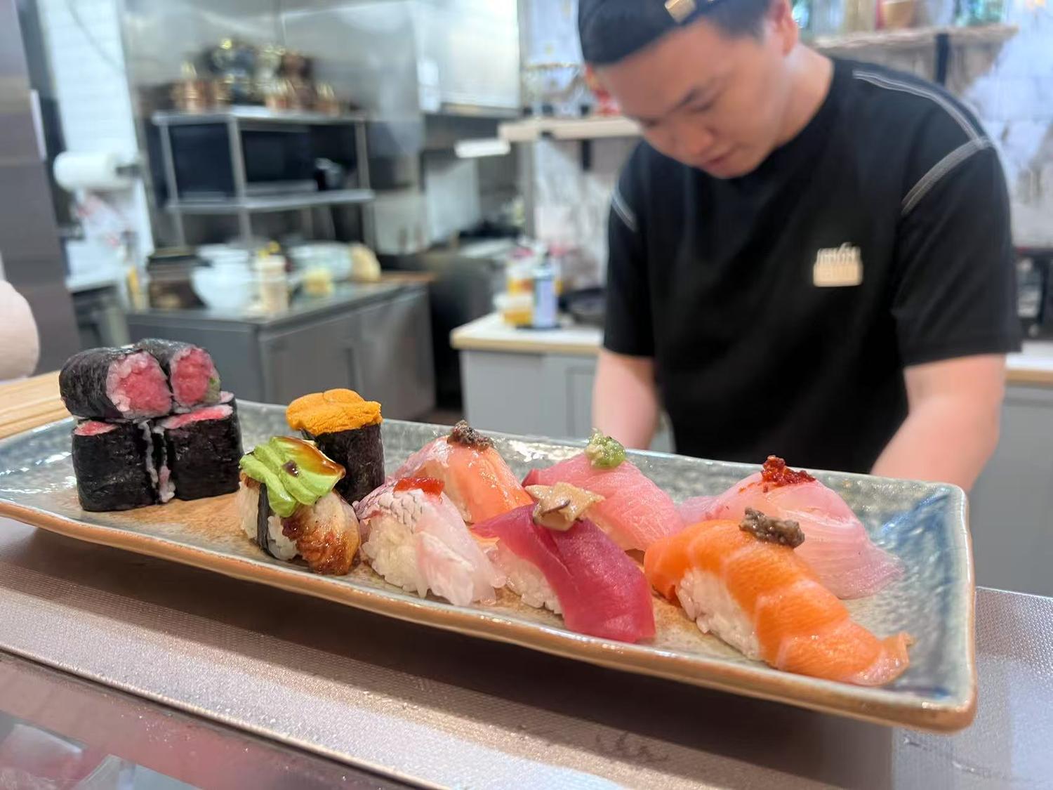 Assorted sushi platter with various fresh fish, including rolls and nigiri, presented at a counter.