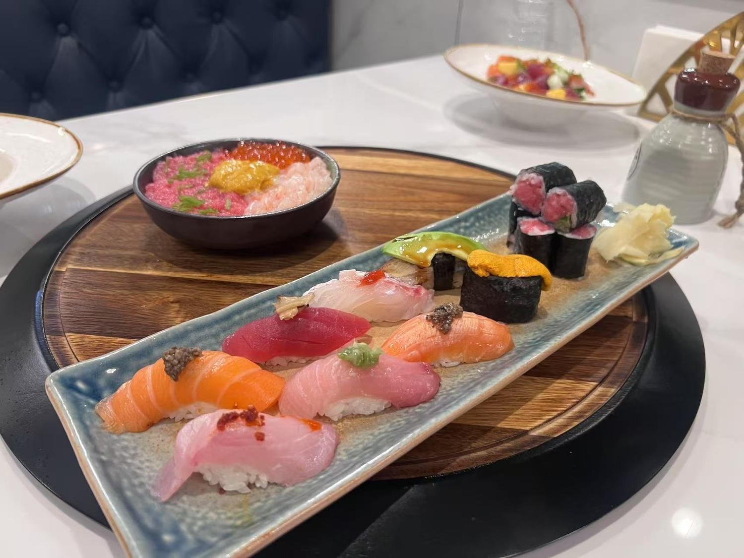 Sushi and sashimi set featuring assorted nigiri, rolls, and a bowl of seafood - topped rice.