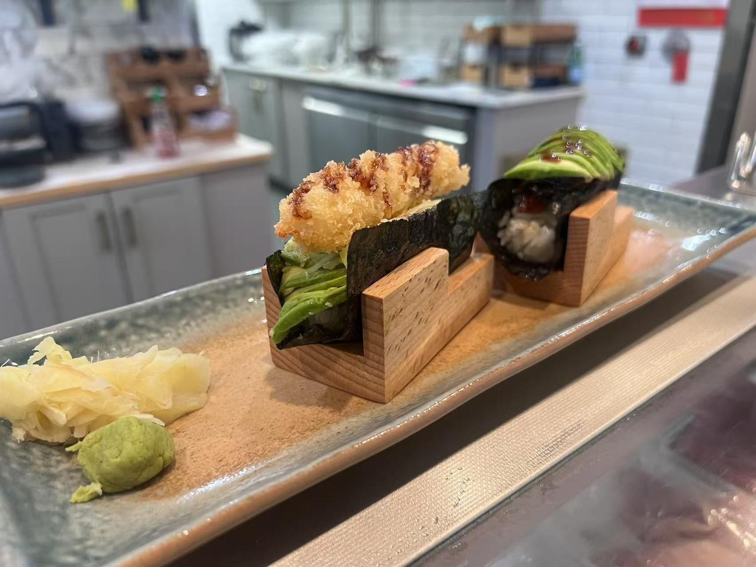 Two pieces of creative sushi with fried ingredients and avocado, served with pickled ginger and wasabi.