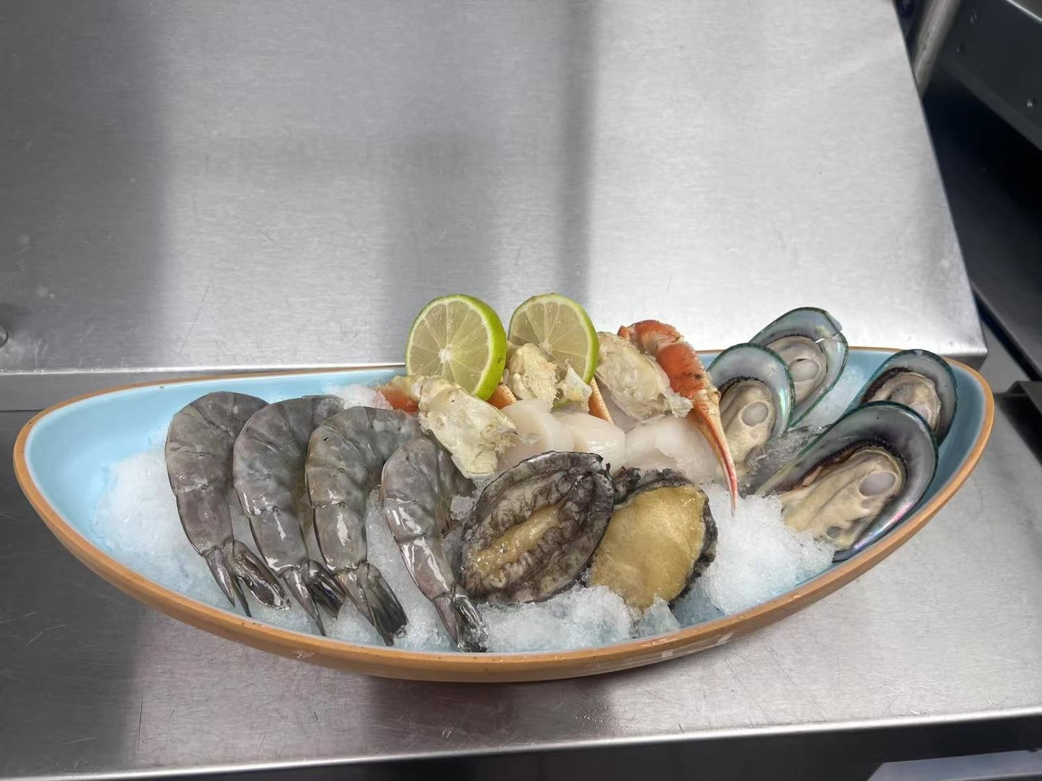 Seafood platter on ice, including shrimp, abalone, mussels, and crab, garnished with lime.