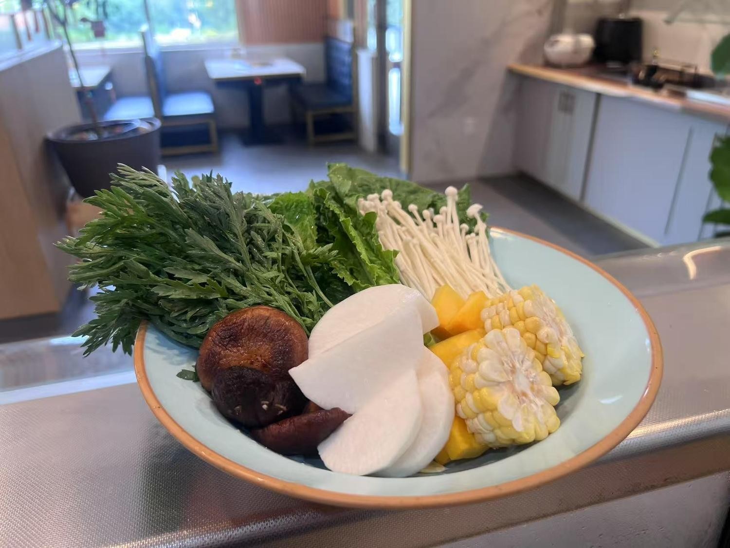 A plate of assorted fresh vegetables like greens, mushrooms, corn, ready for cooking.