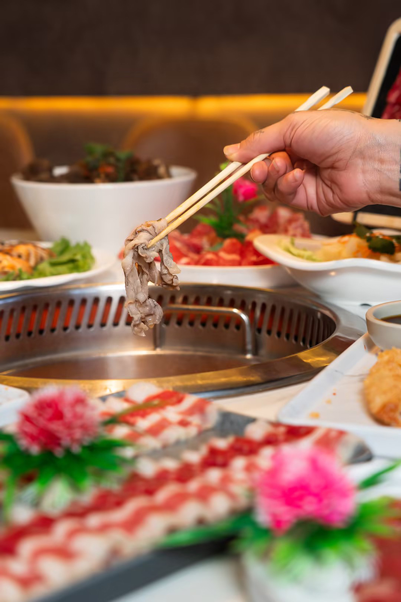 Chopsticks lifting a slice of cooked meat from pot at Happy Lamb Hot Pot Restaurant in Austin