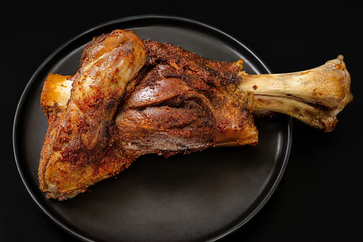 A roasted lamb shank seasoned with spices on a black plate at Happy Lamb Hot Pot Restaurant in Austin