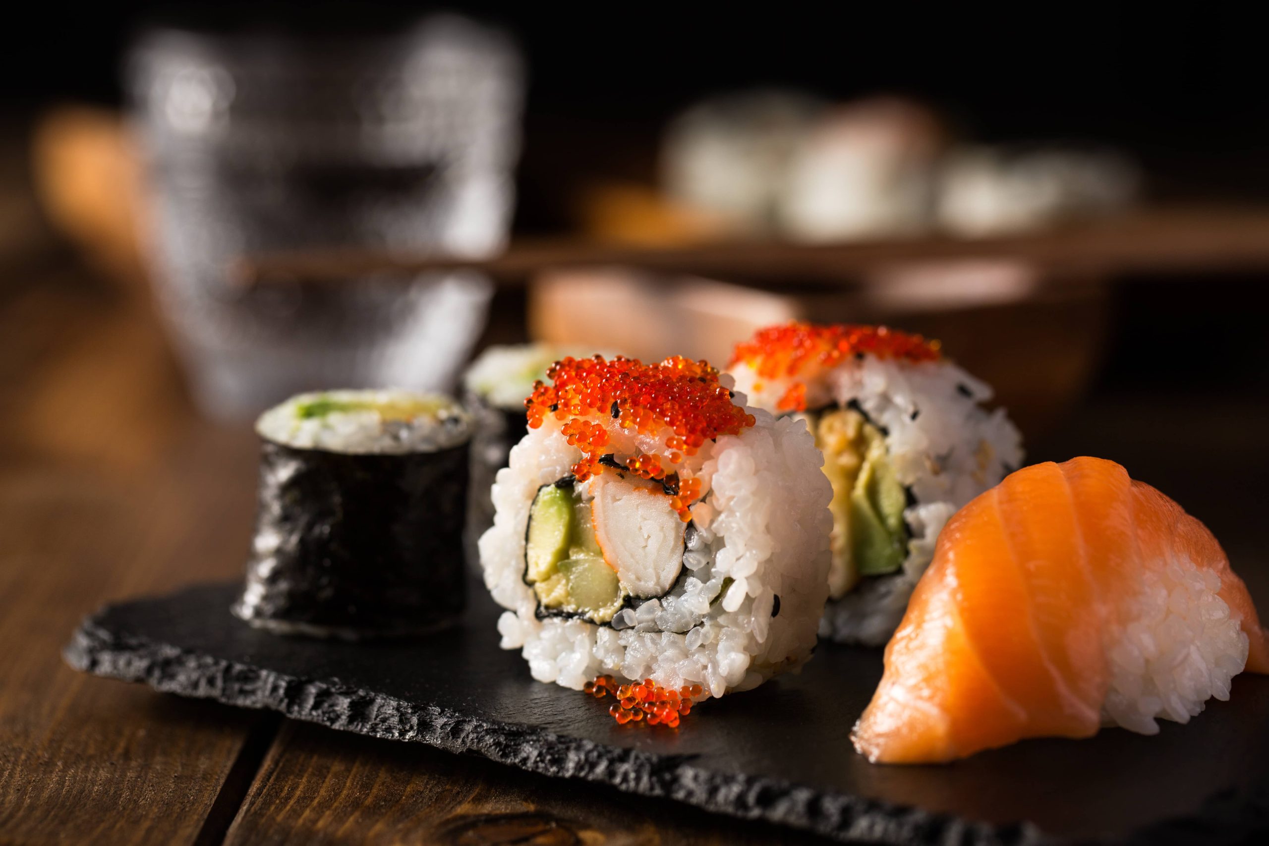 Assorted Japanese sushi rolls with shrimp, avocado, cucumber, fish roe, and salmon nigiri on a black slate plate