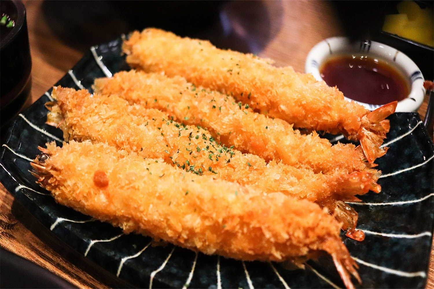 Fried shrimp tempura on a black plate with dipping sauce