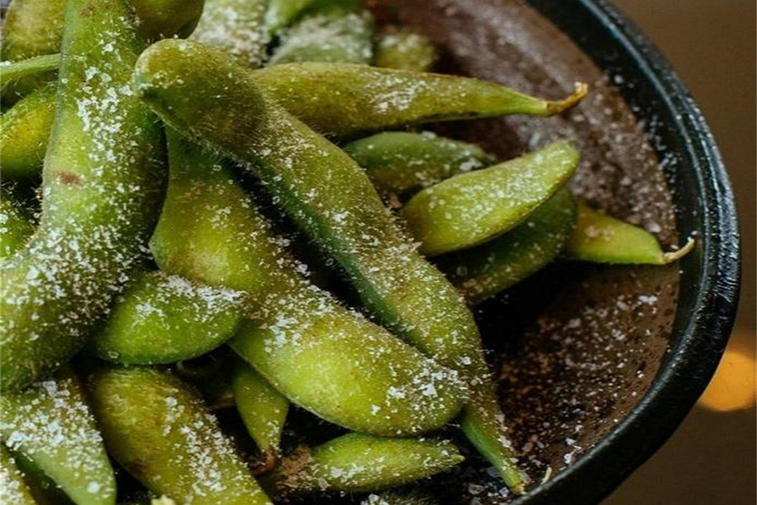 Salted edamame pods in a dark bowl close-up
