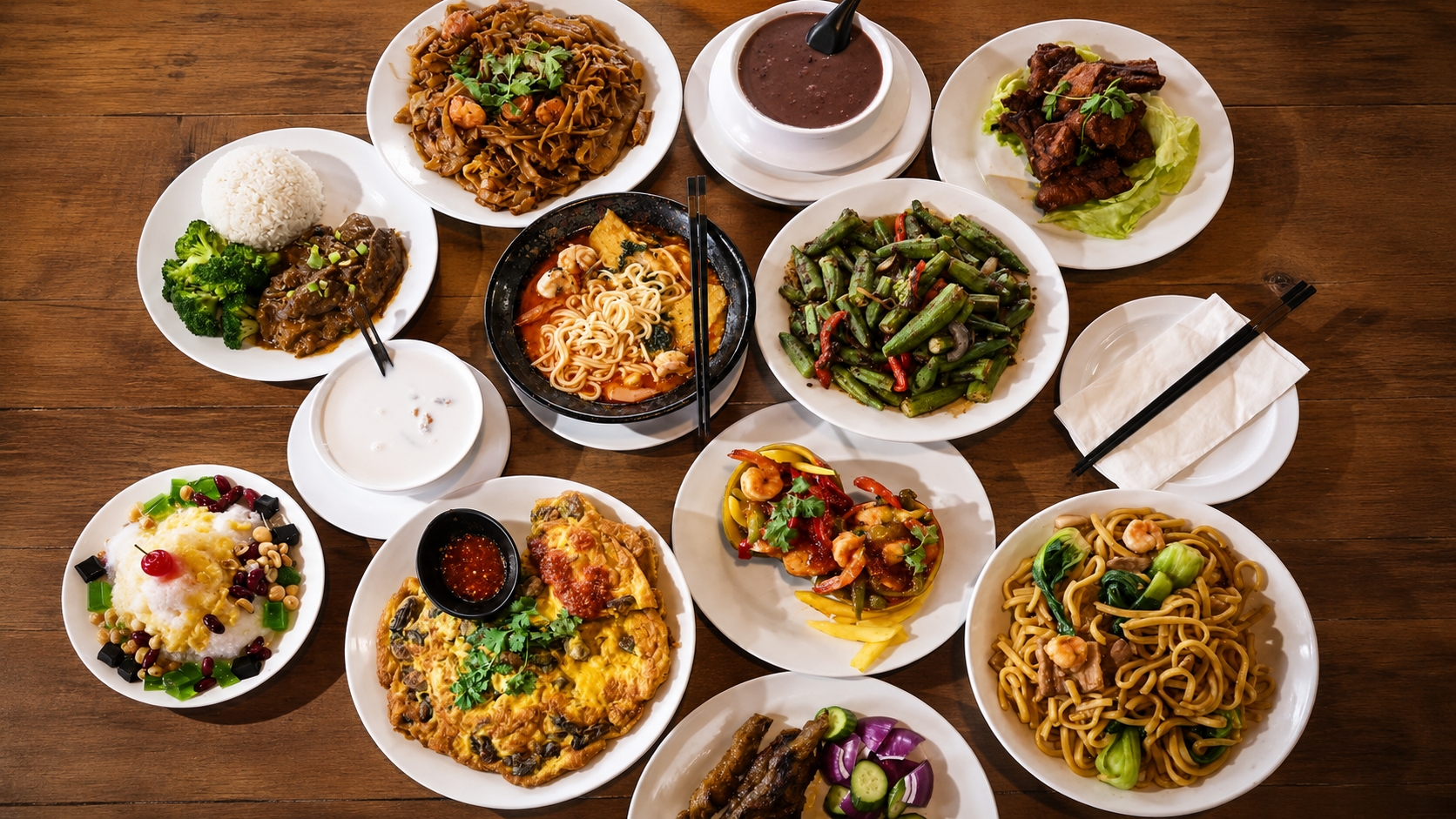 Overhead spread of Asian dishes including noodles, curry rice, soup, okra, skewers, omelet, shrimp, and dessert at Hawker CO, a Malaysian Restaurant in Las Vegas