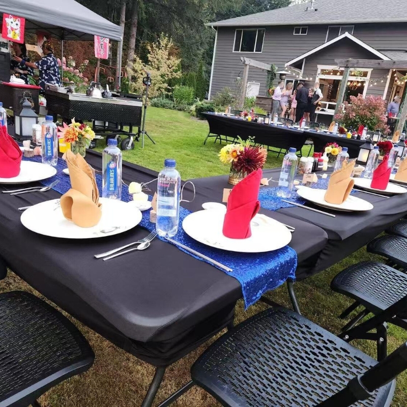 Outdoor dining area with decorated tables, black tablecloths, blue runners, and flowers.