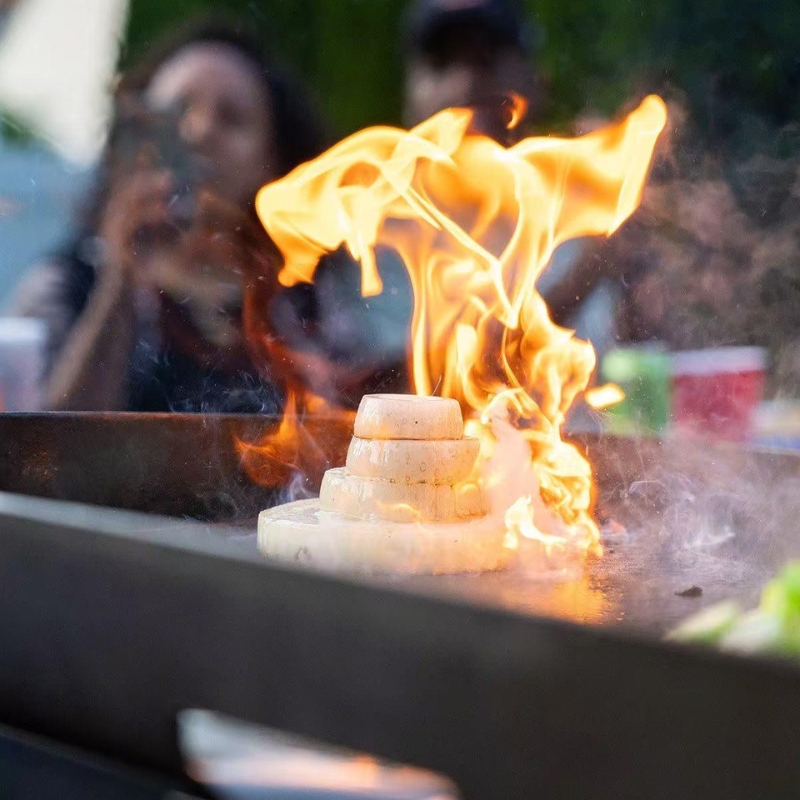 Onions flaming on hibachi grill, with people in the background.