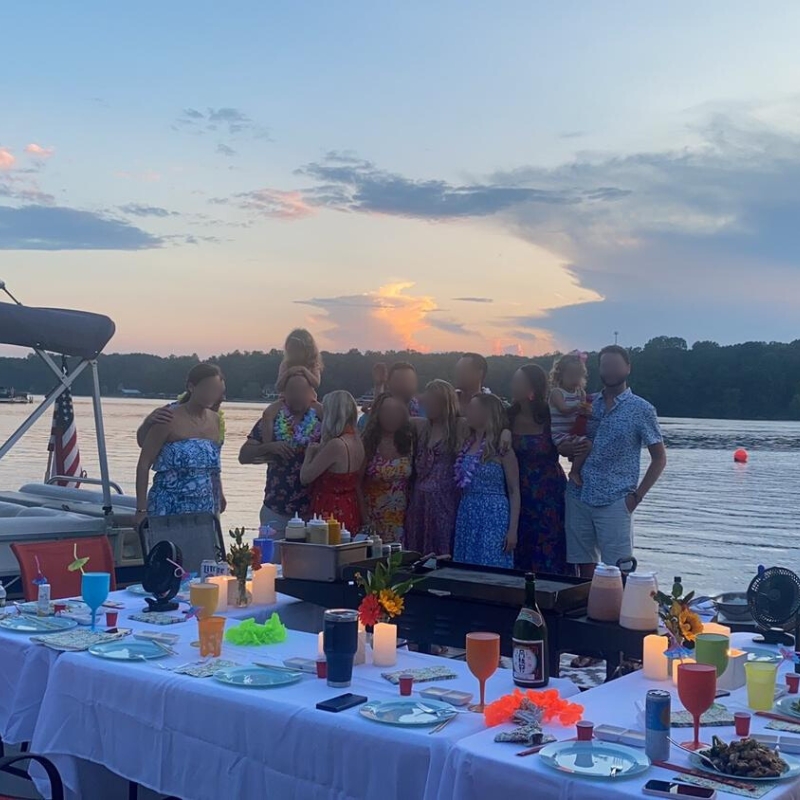 Lakefront hibachi party at sunset, people gathered by tables with decorations.