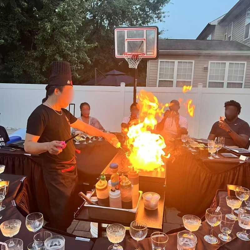 Hibachi-At-Yours-Hibachi-Restaurant-Chef-Performing-Flame-Cooking-Outdoor-Columbia Chef cooks with flames, guests watch at Hibachi At Yours,a Hibachi Restaurant in Columbia.