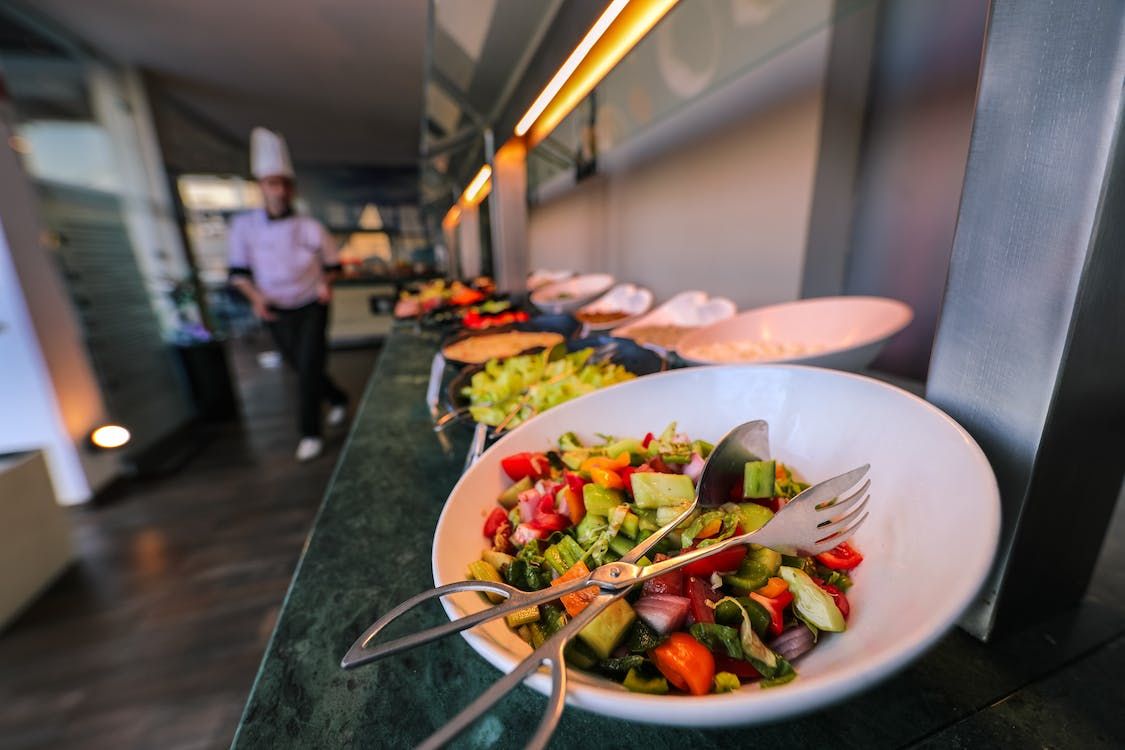 Buffet line with fresh salad, vegetables, and chef in background.