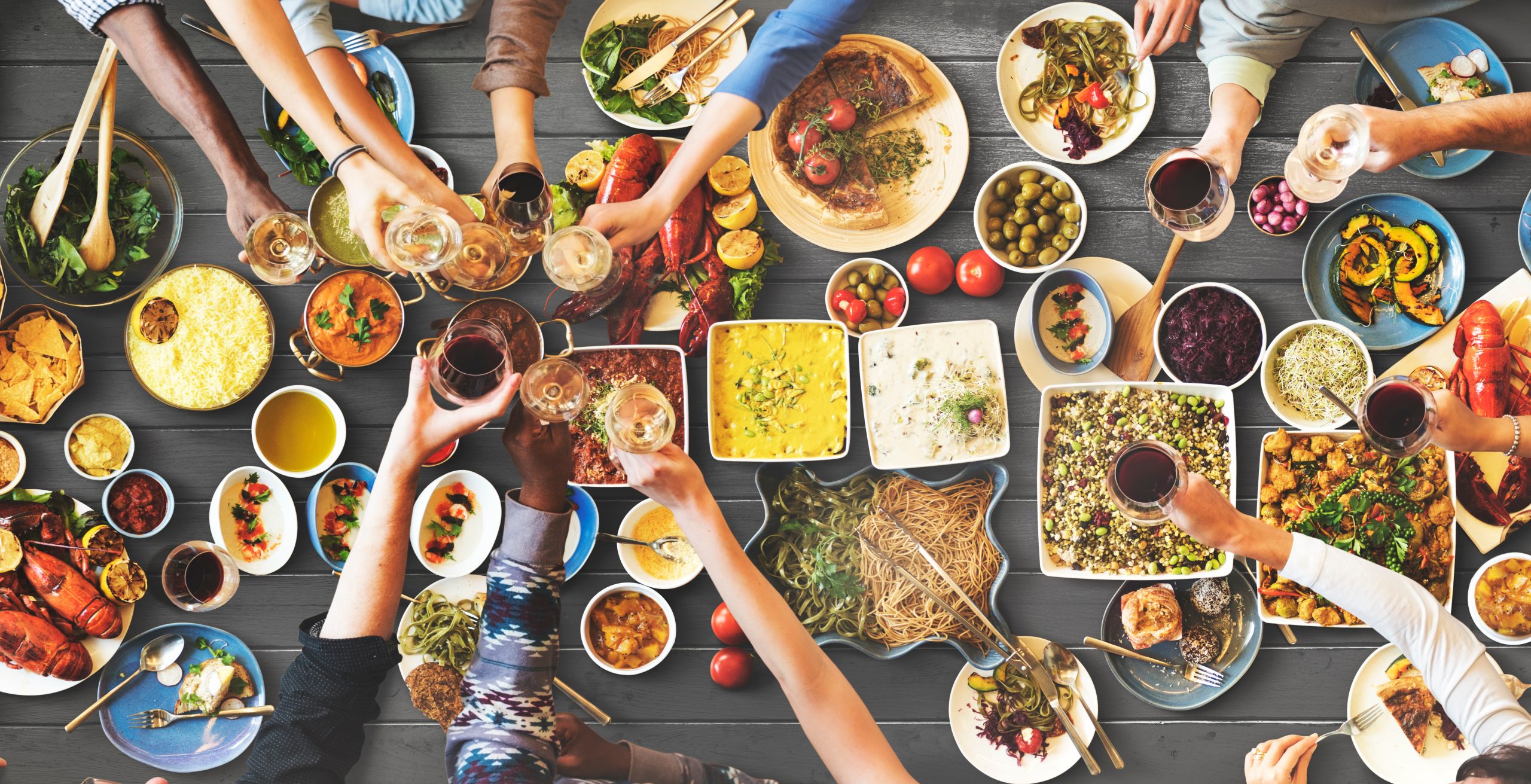 Diverse group sharing a festive meal with colorful dishes and wine glasses.