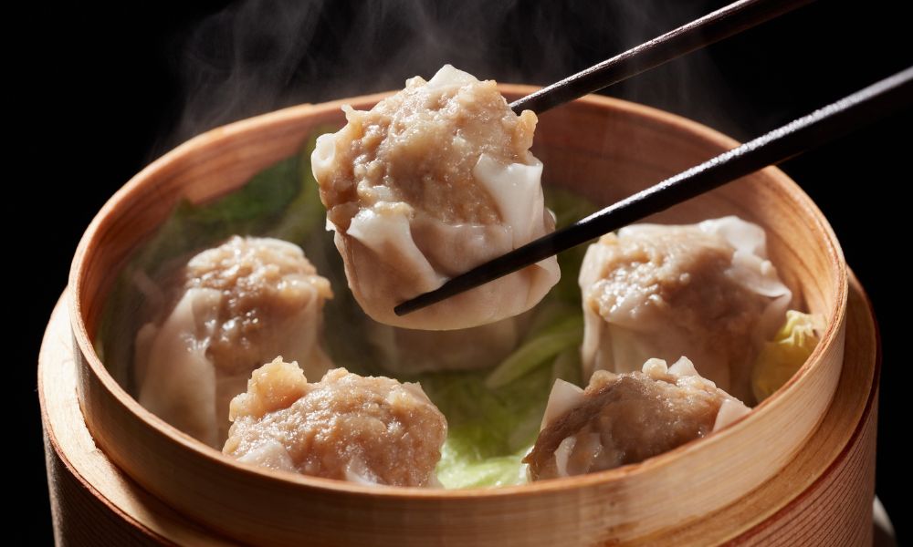 Steamed siu mai dumplings lifted by chopsticks from a bamboo steamer at High Five Asian Street Food, a Asian restaurant in Ormond Beach