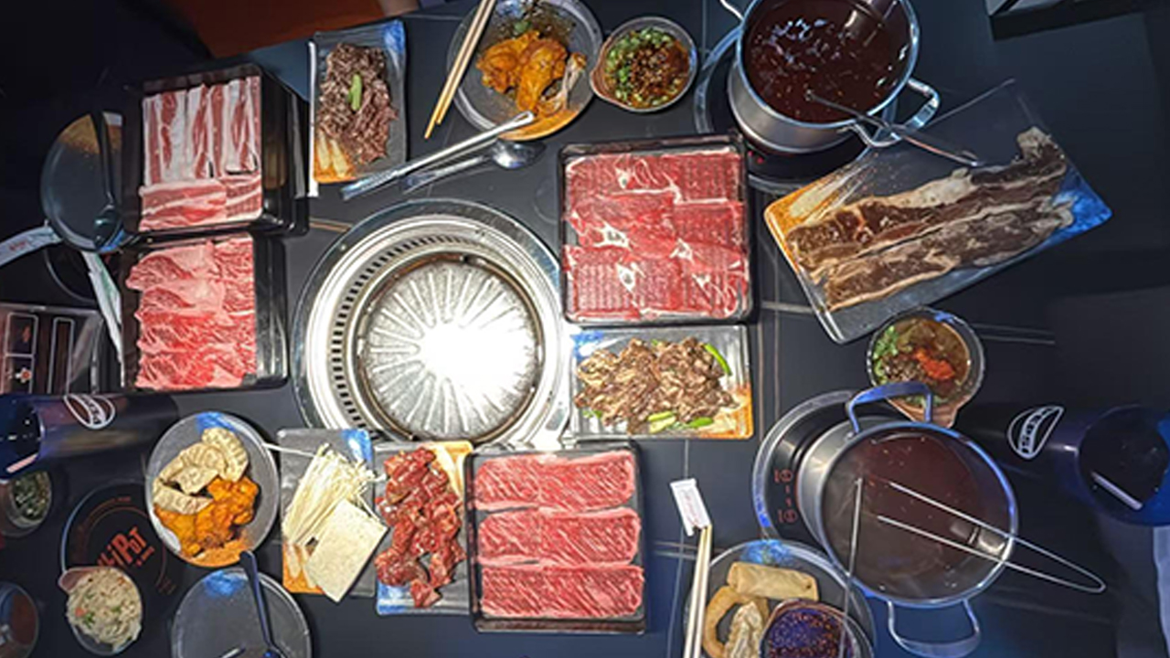 An overhead view of a lavish Korean BBQ feast, featuring multiple meat platters, side dishes, and two hot pots on the table.