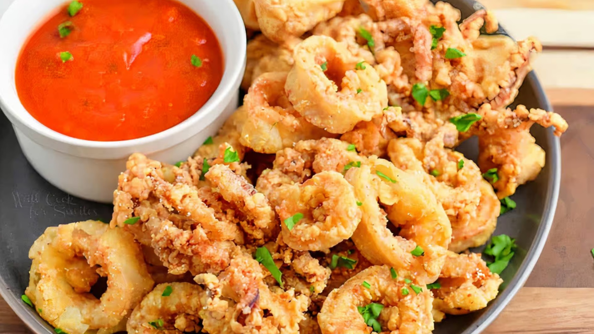 Crispy fried calamari rings with red dipping sauce on a dark plate