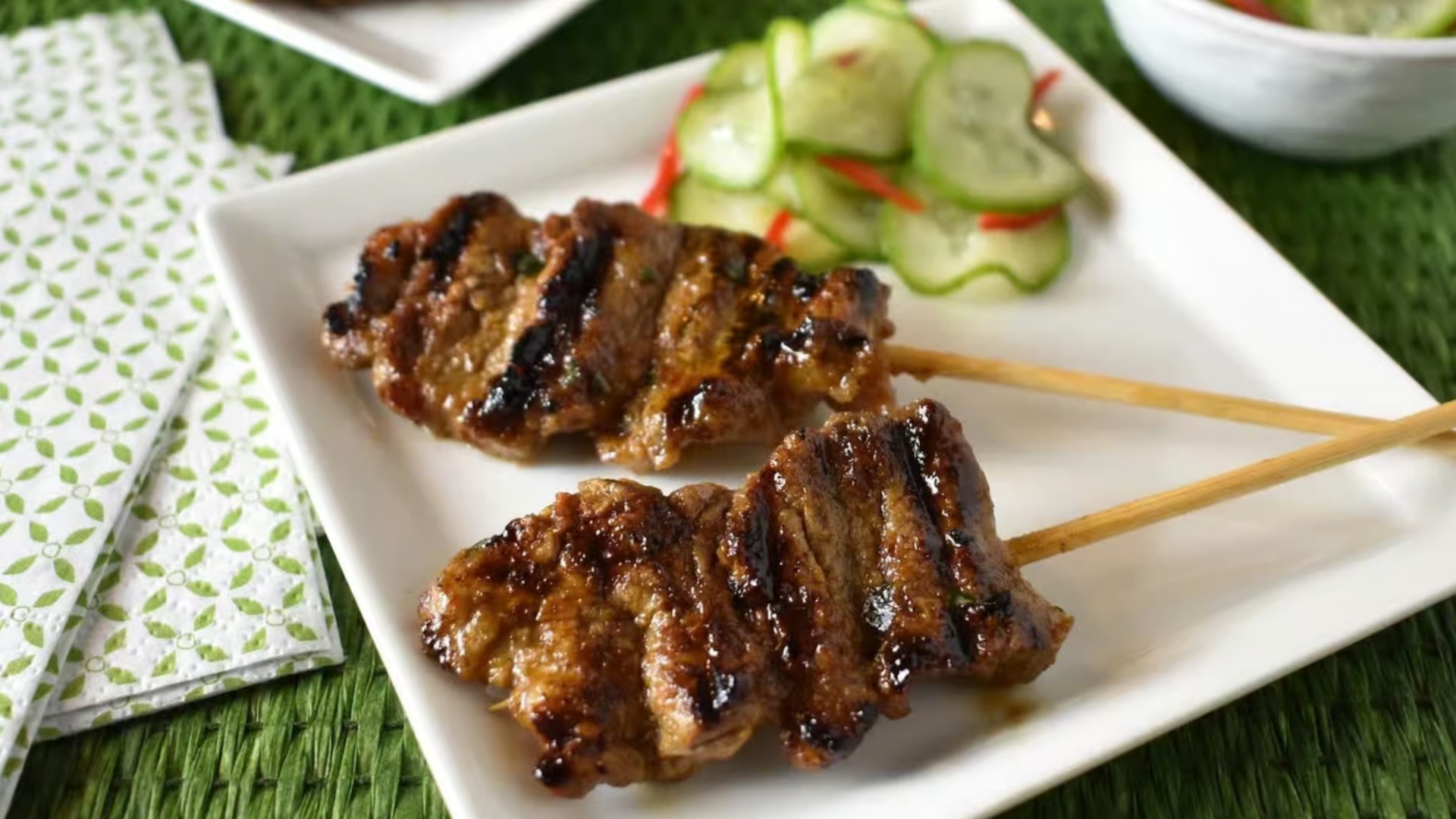 Glazed meat skewers with cucumber salad on a white plate