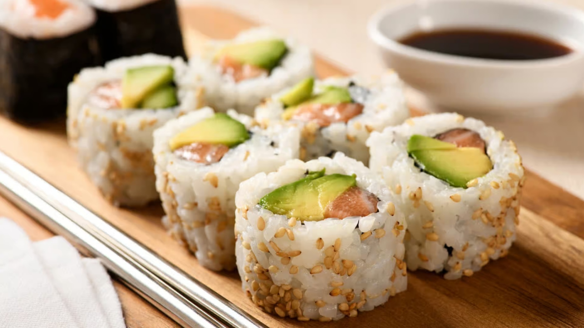 Sesame-coated sushi rolls with avocado and salmon on a wooden board