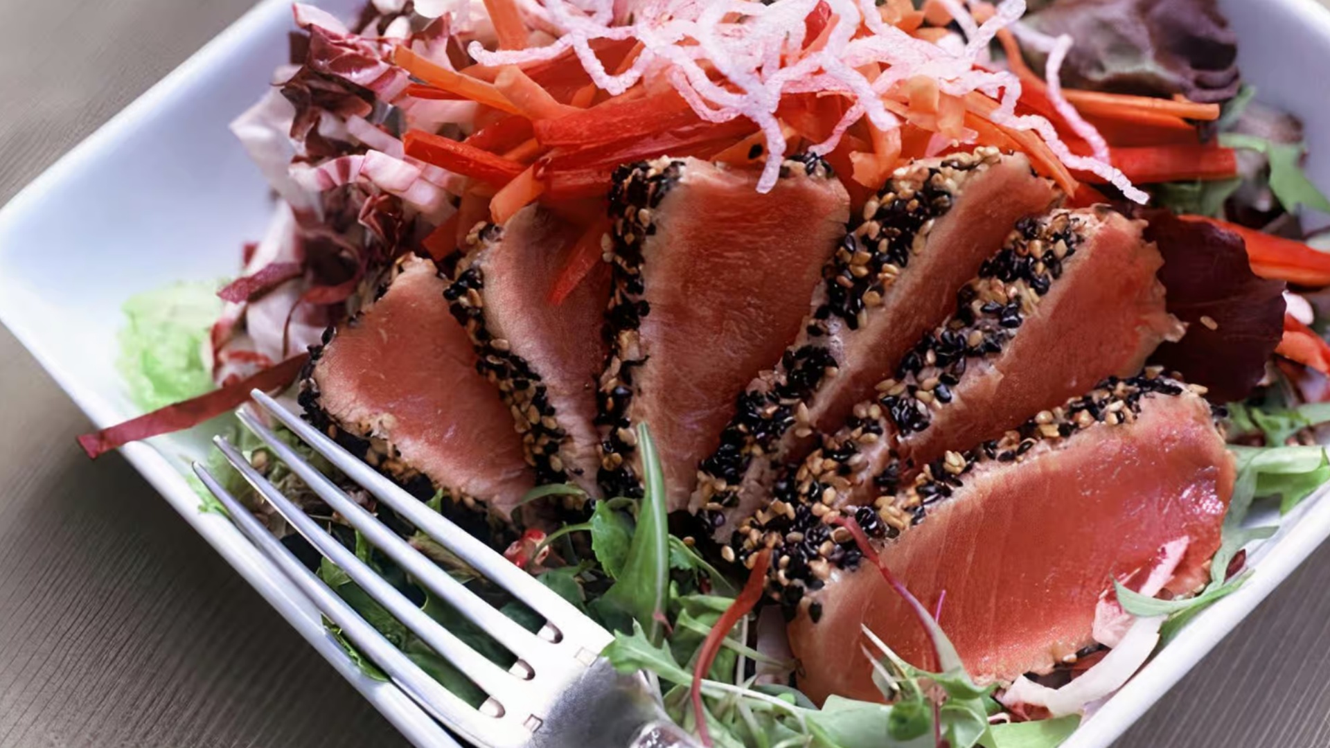 Sesame-crusted seared tuna slices over a fresh vegetable salad