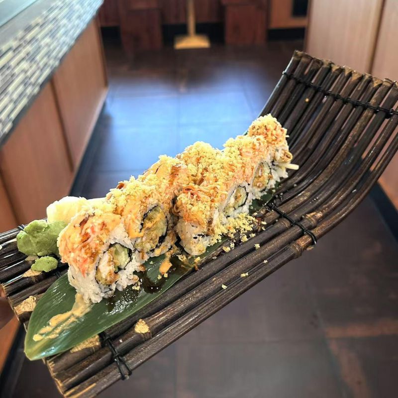 Hokkaido-Ramen-&-Sushi-Japanese-Restaurant-Crispy-Topped-Sushi-Roll-Lubbock Sushi roll topped with crispy bits, served on a bamboo - like tray.