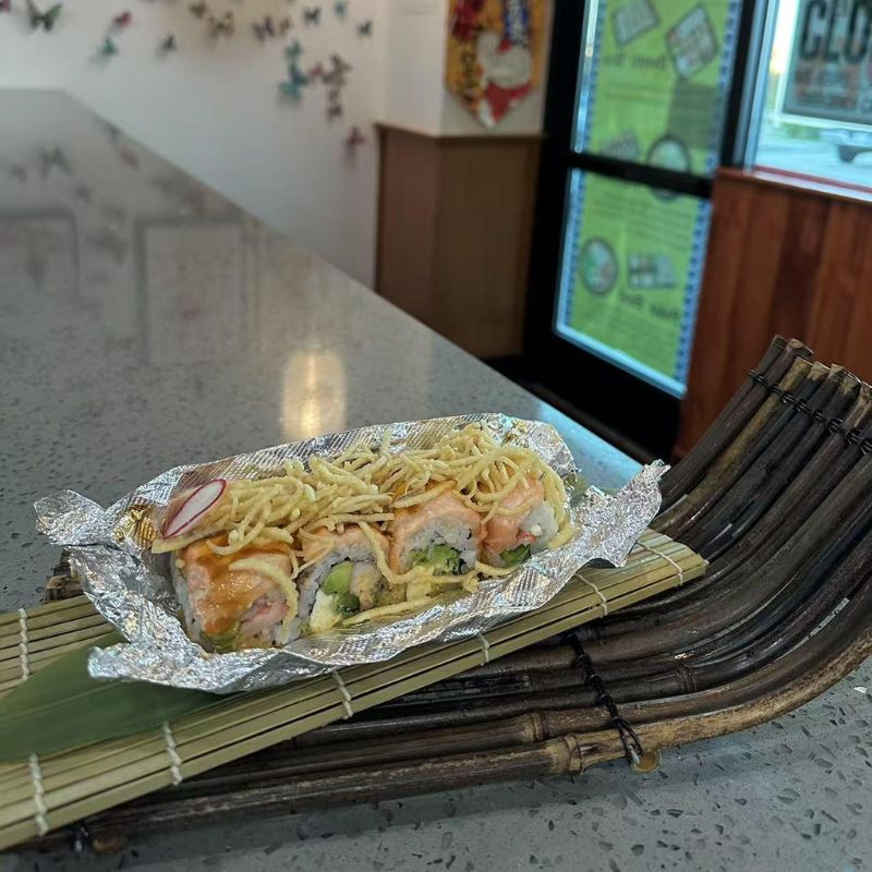 Hokkaido-Ramen-&-Sushi-Japanese-Restaurant-Fried-Noodle-Topped-Sushi-Lubbock Sushi roll garnished with fried noodles, wrapped in aluminum foil.