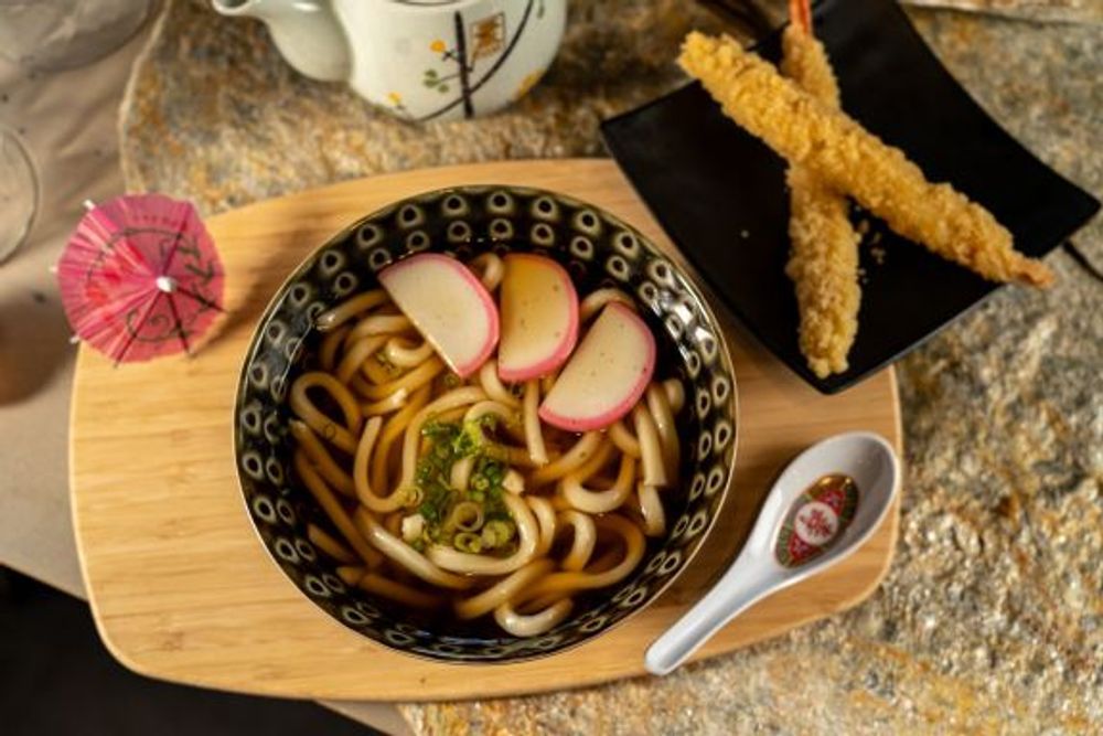 Classic udon noodle soup paired with two crispy tempura shrimp on side plate at Hokkaido Sushi Bar, a Japanese Restaurant in Vancouver