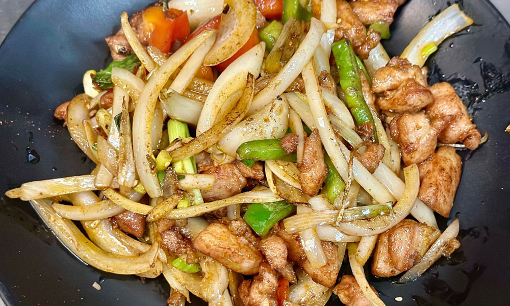 Stir-fried chicken with onions, peppers, and scallions on a black plate