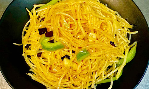Stir-fried shredded potato with chili and scallions on a black plate
