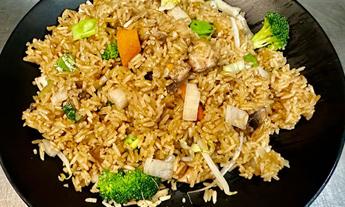 Chicken fried rice with vegetables and broccoli on a black plate
