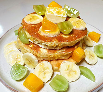 Fluffy fruit-topped pancakes with banana, mango, grapes, butter at TOZZARELLA, a Dessert restaurant in College Point