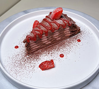 Chocolate crepe cake slice with strawberry sauce, cocoa dust at TOZZARELLA, a Dessert restaurant in College Point