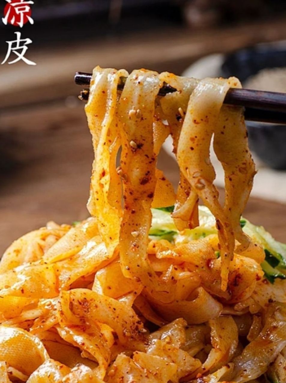 Chopsticks lifting spicy cold noodles with cucumber in a bowl