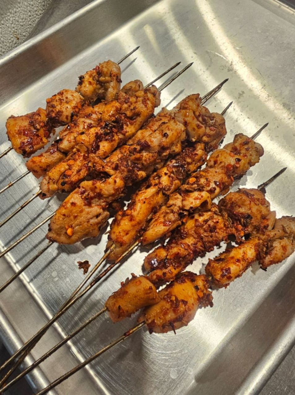 Grilled chicken skewers coated in chili and cumin on a metal tray