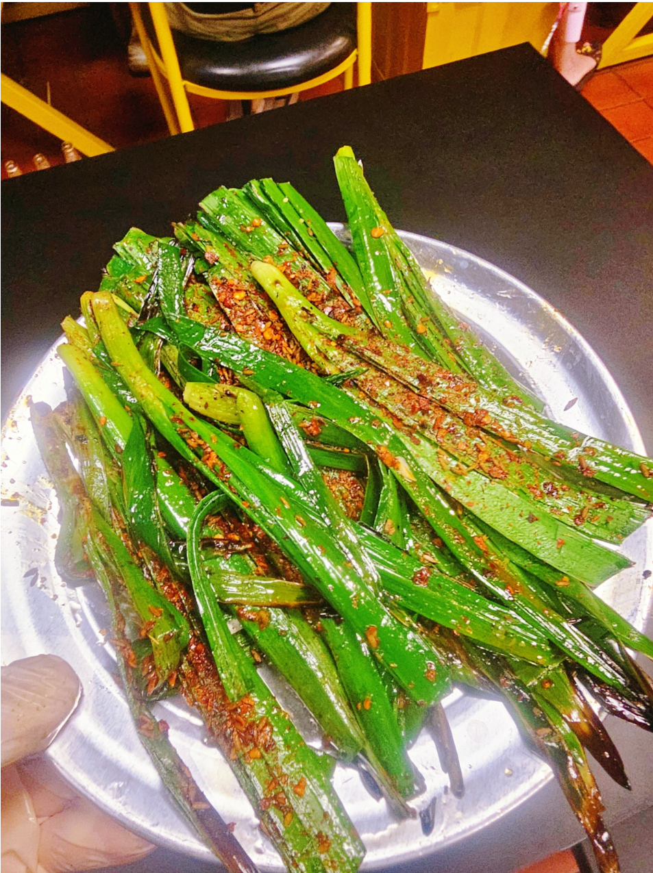 Grilled chives seasoned with chili flakes on a metal plate